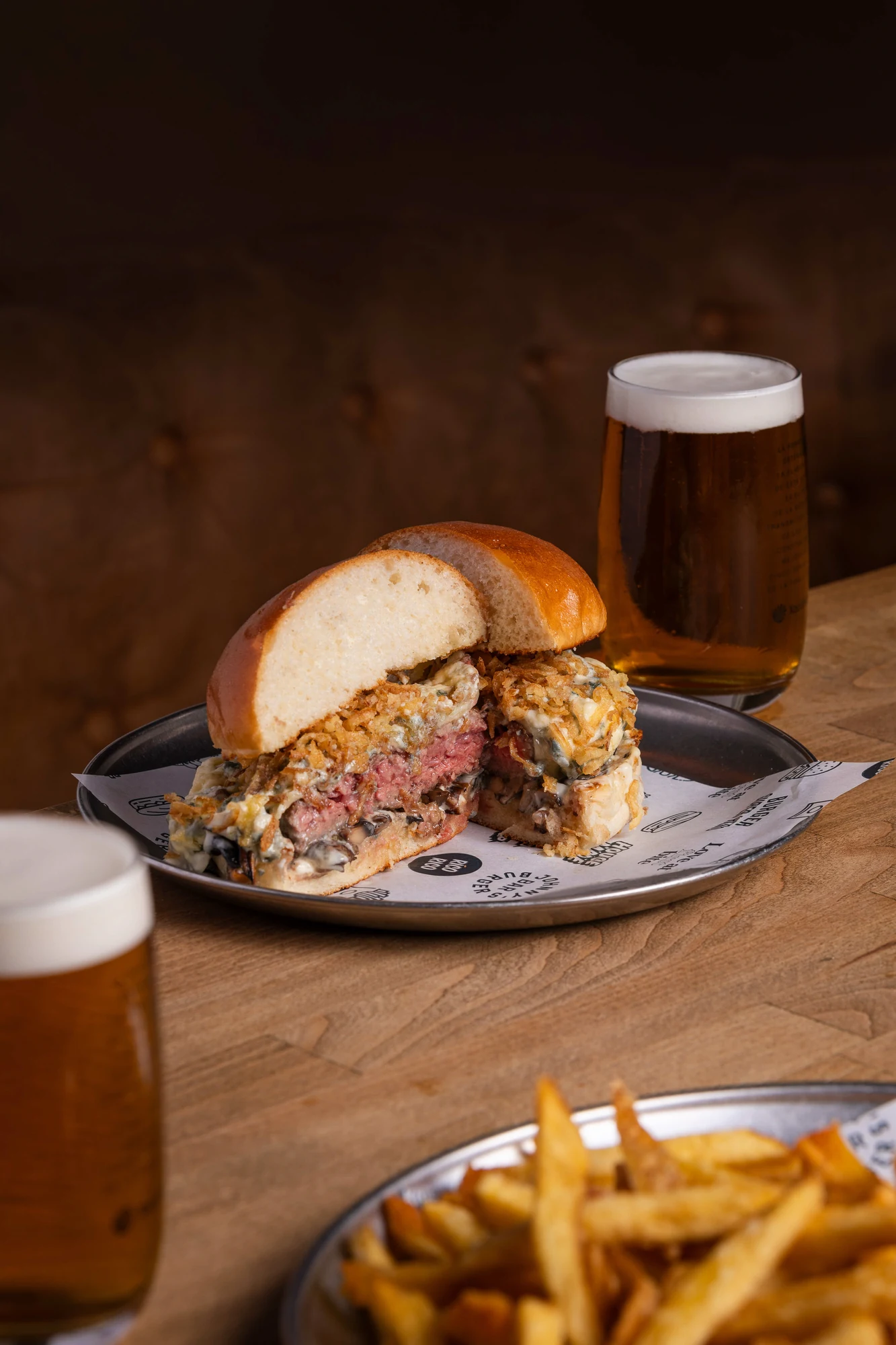 Burger cortada por la mitad con cebolla crujiente, con cerveza y patatas